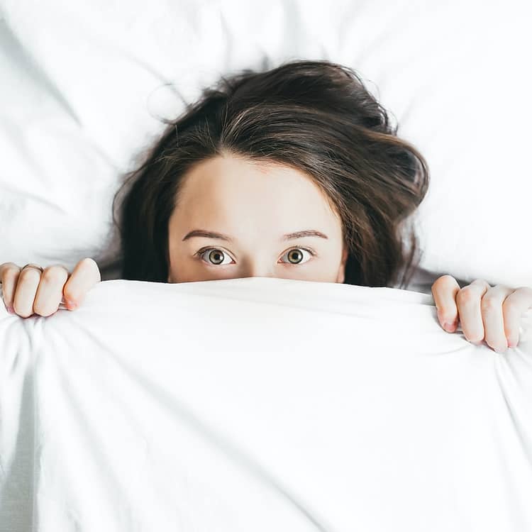 a girl staring at the camera in fear while the lower half her face is covered with a bedsheet